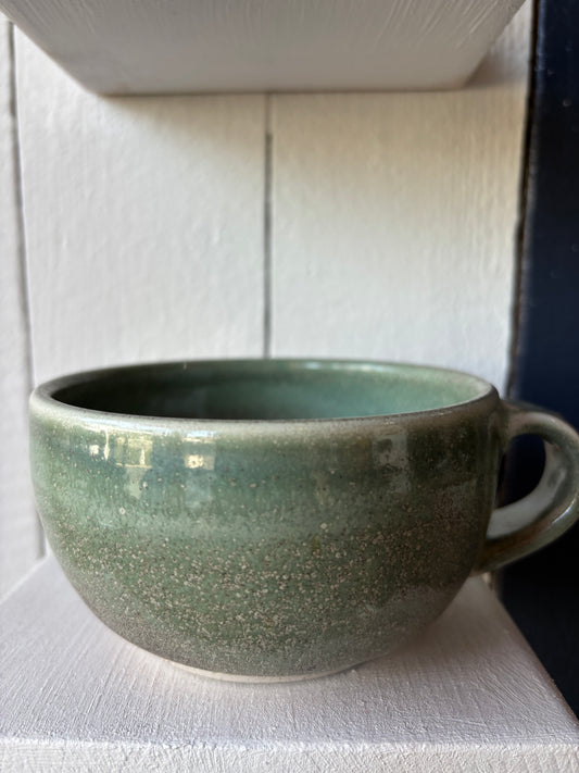 Green ceramic bowl with a handle on a white surface