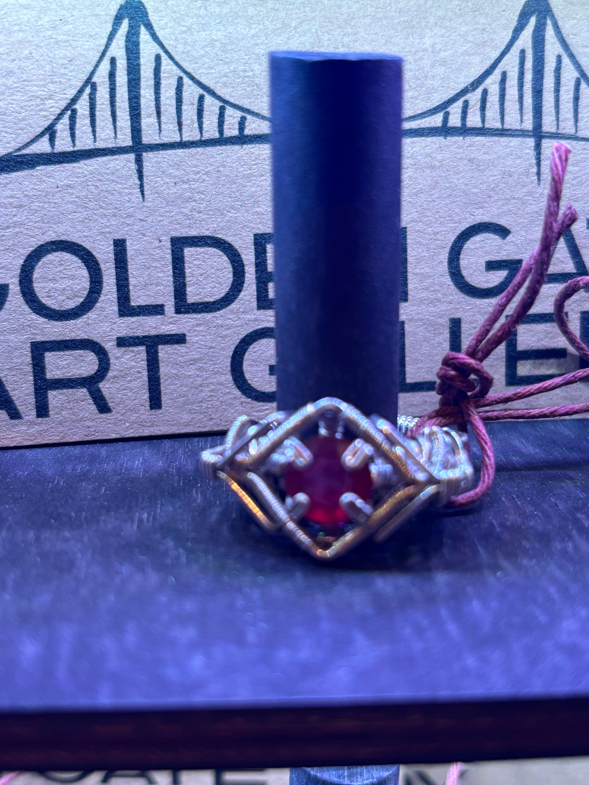 Silver ring with a red gemstone on a blue surface with 'Golden Gate Art Glass' branding.