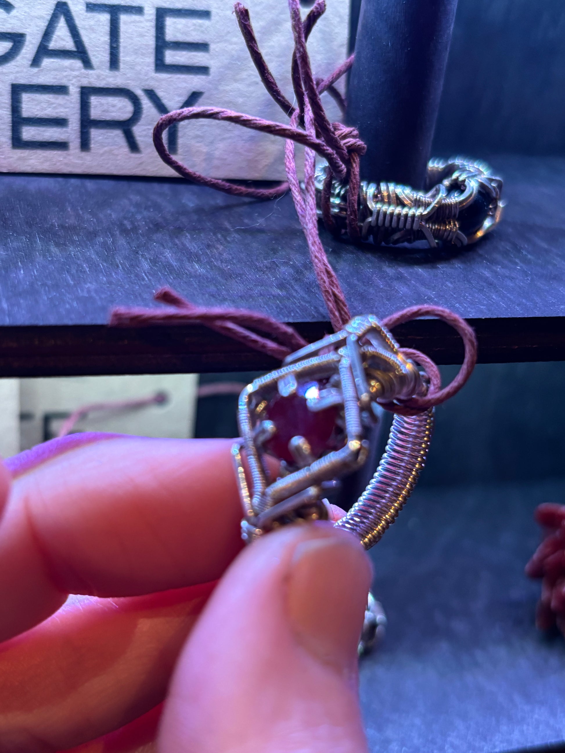 Close-up of a hand holding a silver pendant with a red gemstone against a blurred background.