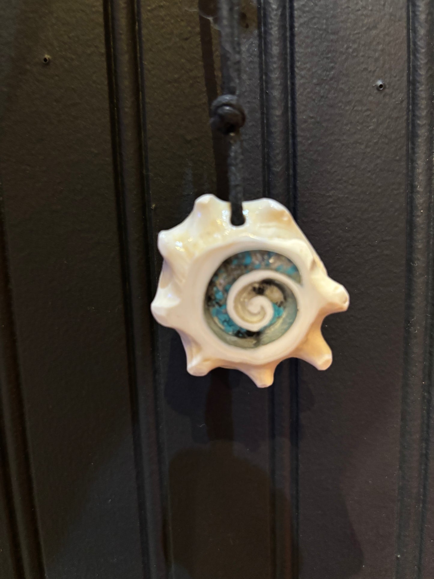 Decorative seashell pendant necklace with a spiral design on a black background