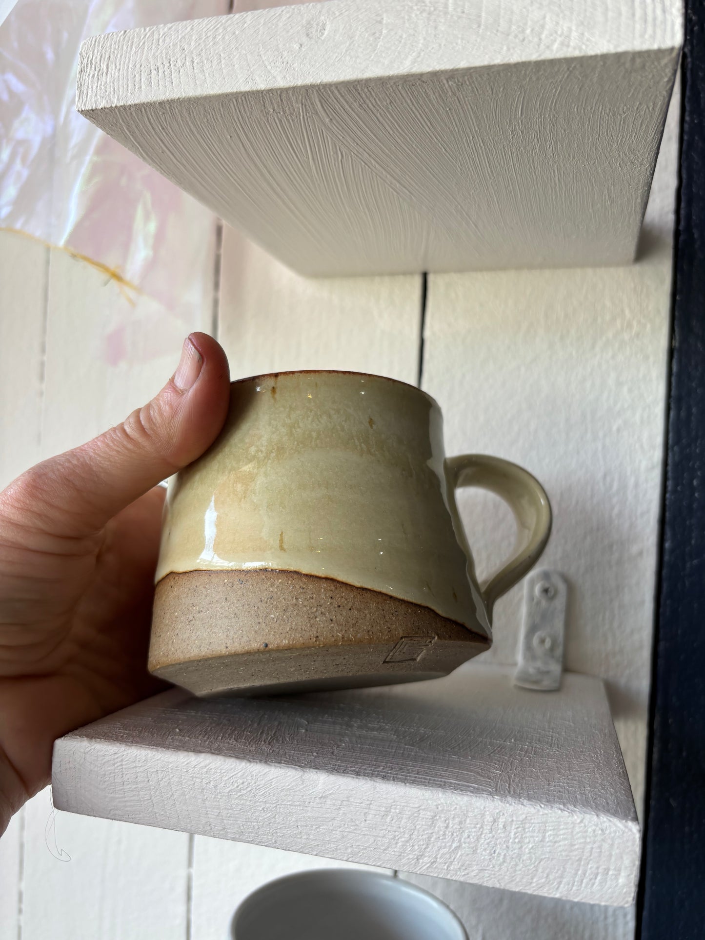 Hand holding a ceramic mug on a wooden shelf