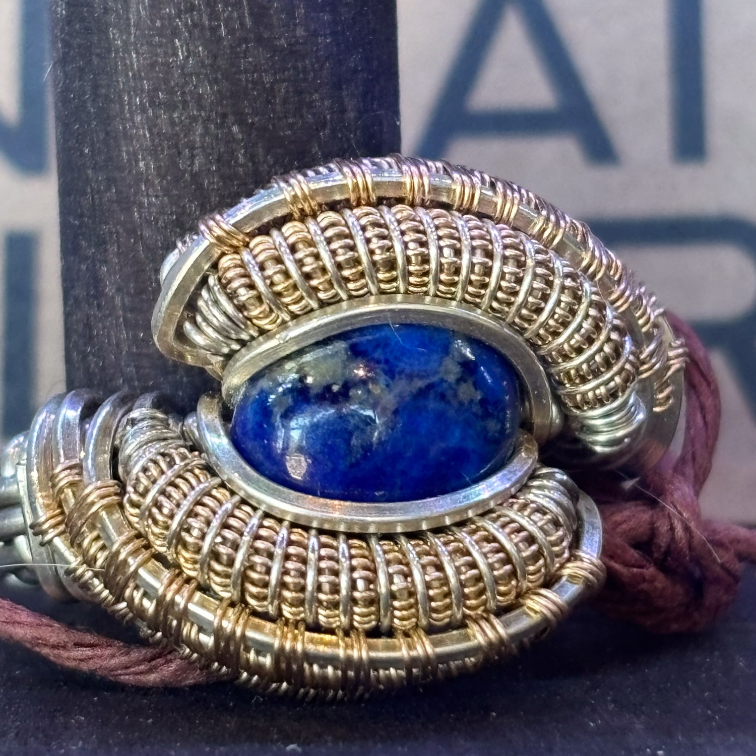 Gold and silver wire wrap ring with a blue lapis stone on a dark background