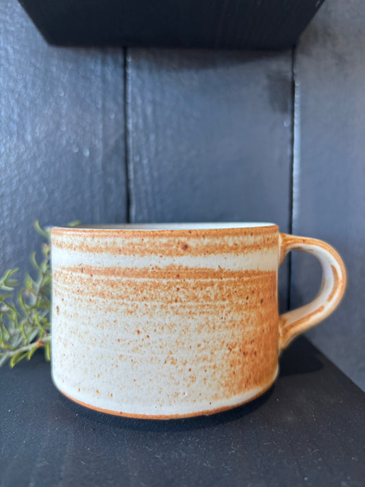 Ceramic mug with brown and white speckled design on a dark surface.