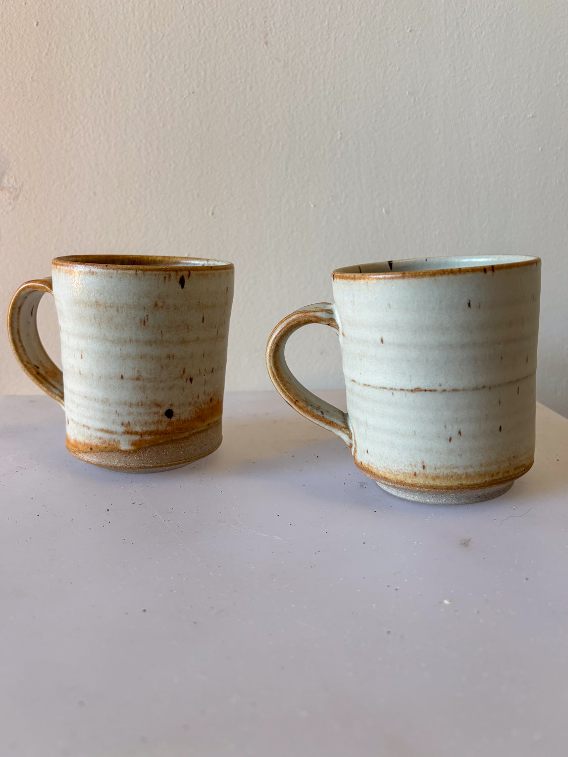 Two ceramic mugs with rustic finish on a plain background