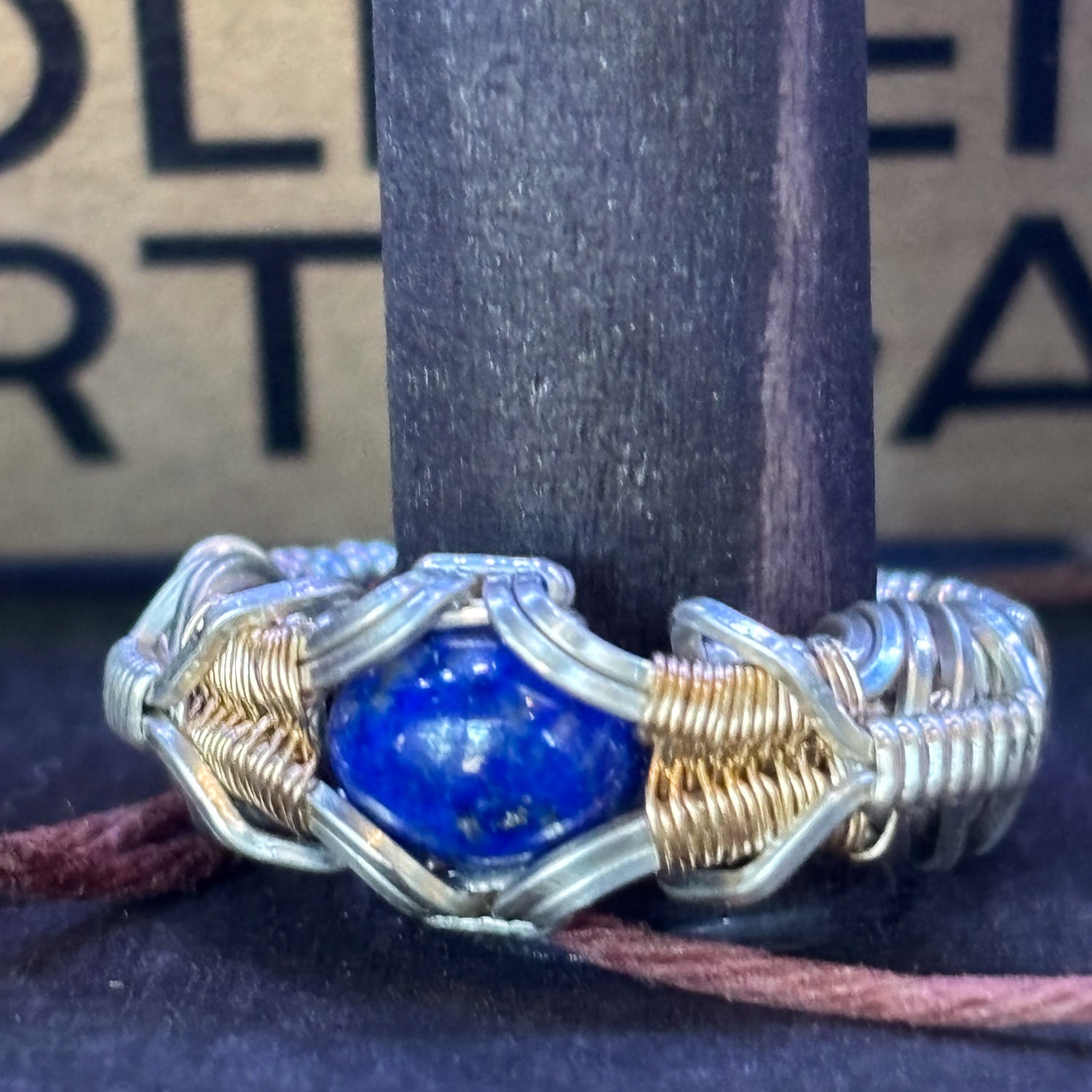 Silver and gold wire-wrapped ring with a blue stone on a dark background