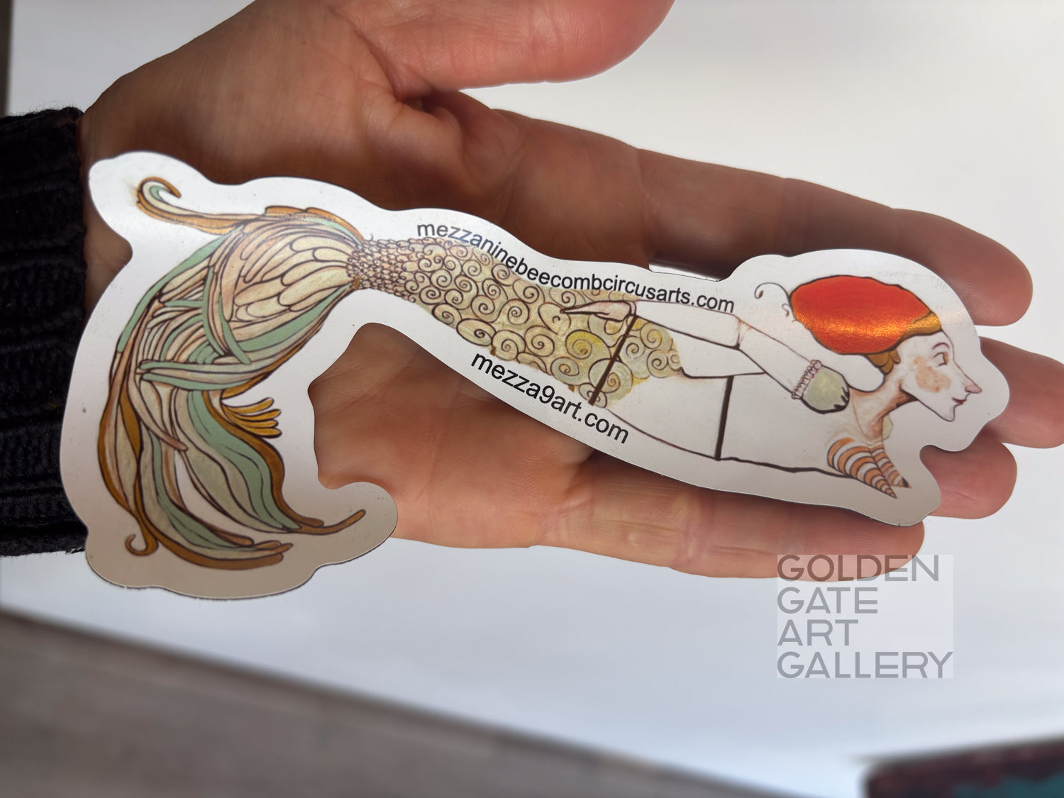 hand holding a colorful mermaid magnet with mezza9 branding on it